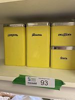 Front view of four yellow metal canisters labeled sugar, flour, coffee, and tea with chrome lids.