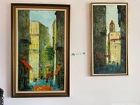 Two original paintings by R. Diaz displayed on wall showing street view scenes in colorful tones.