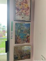 Set of three framed paintings by Andrea Stoian showing floral and landscape themes hung vertically
