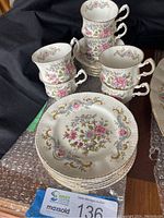 Photo of stacked teacups with matching saucers and side plates showing floral and gold design.