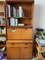 Full view of teak cabinet showing upper bookshelf with books, fold-down desk closed, drawer, and lower cabinet doors.