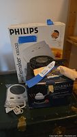Photo showing Philips waffle maker in box, fondue set box, and two electric pot warmers with cords on table.