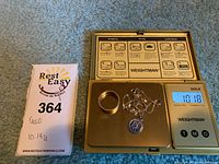 Ring, rope chain, and round pendant on digital scale showing total weight alongside seller’s hand-written tag.