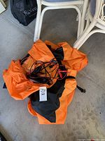 Orange and black bike cover loosely folded with charger cables on top, gray floor background