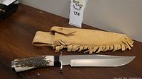 Overview of knife with bone handle and suede sheath on wooden surface