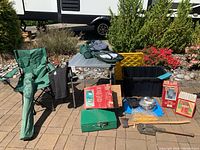 Wide shot of camping lot items on paved ground showing chair, table, cooler backpack, camp stove, and assorted accessories