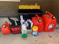 Full view of the lot showing gas cans, cleaning products basket, black and yellow tote, and work bag