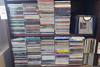 Front view of two wooden shelves holding audio CDs in jewel cases and one binder