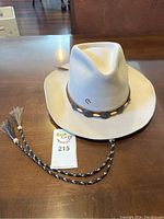 Light beige Charlie Horse western hat with leather band and tassels on a wooden table.