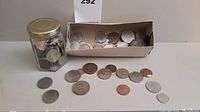 Coins in glass jar and cardboard tray with some laid out on surface, showcasing mix of sizes and metal tones.