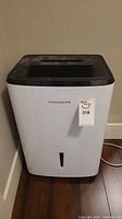 Front view of white Frigidaire portable air conditioner with black top and front water level indicator.