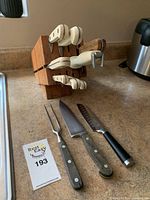 Front view of wooden knife block holding ivory-handled knives with three loose utensils on countertop