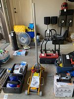 Garage setting photo showing the yellow aluminum race jack, a fan, and toolboxes surrounding it with other automotive equipment visible.