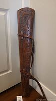 Full view of brown leather rifle case holster showing length, strap, and carved floral leaf tooling details.