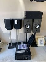 Two small black Energy satellite speakers on silver stands next to two gray speakers on black stands with Yamaha amplifier below