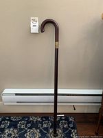 Full view of dark polished wooden walking stick with curved handle and brass band.