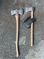 Two axes shown lying on ground: one double-sided with long handle, other single-sided with Kurts black cover on head.