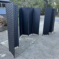 Three black four-panel room dividers arranged outdoors with visible woven pattern and folding hinge mechanism.