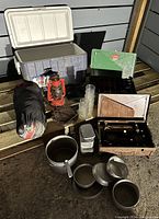 Full view of camping lot items showing sleeping bag, cooler, red lantern, stoves, cookware, and plastic cups