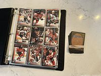 View of binder opened to a page with New Jersey Devils hockey cards and a rubber-banded stack of Magic: The Gathering cards on a counter.