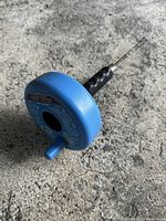 Blue canister auger drain snake lying on concrete surface showing side with instructions and specs.