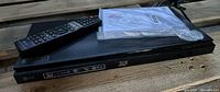 Photo showing black LG 3D Blu Ray player with remote control placed on top and white documentation packet.