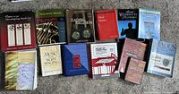 Front face view of 13 music education textbooks spread out on carpet including titles on piano, brass, percussion, conducting, music analysis, and more.