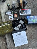 Collection of Star Wars memorabilia including games, action figures, stickers, and VHS tapes displayed on ground