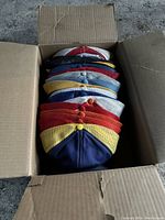 Box of 9 assorted trucker hats stacked vertically showing various colored mesh backs and capped tops.