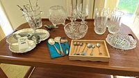 Full lot on wood table showing ice bucket, glasses, bowls, spoons on cloth and tray, and serving forks.