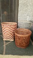 Two woven baskets side by side in front of fireplace screen.