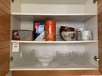 View of shelving unit with various bowls, dishes, and containers including glass bowls, ceramic, and tins