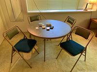 Full view of the round card table with four folding chairs around it in a room under window.