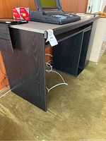 Black office desk viewed from the front and side showing the main top surface and keyboard sliding shelf underneath.