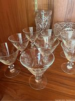 Six etched martini glasses on wooden shelf with additional glass items behind.