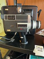 Side view of Canon Super 8 movie camera showing manual zoom lever and lens assembly with manufacturer labels. Camera mounted on small tripod.