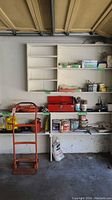 Wide view of garage shelving with hardware and tools showing paint cans, red toolbox, and orange dolly cart