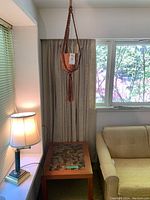 Macrame plant hanger hanging above the tile inlaid wooden table, with a lamp and sofa nearby