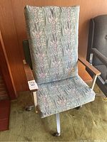 Front view of high back office chair with floral fabric upholstery showing wooden armrests and caster wheels on green carpet.