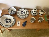 Full view of the dishware set including plates, bowls, coffee cups, creamer jug, serving platter, and ceramic violin-shaped box on wooden table.