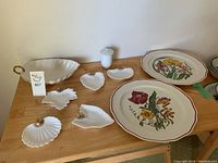 Wide view showing two large Villeroy & Boch plates with floral patterns and an assortment of white porcelain serving dishes including a lidded container and small shaped dishes.