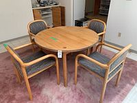 Photo showing the round wooden table with four upholstered chairs arranged around it on a pink carpet.