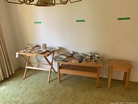 Three solid wood tables arranged in a room with green carpet. Left: folding tray table with dishes, middle: rectangular coffee table with dishes, right: small square side table.