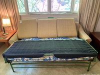 Front view of vintage beige sofa with pull-out bed partially extended showing floral mattress and black cover.