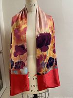 Full view of the silk scarf draped on a dress form showing its floral pattern and solid red silk lining edges.