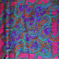 Close-up showing vivid paisley and floral pattern in jewel tones on silk scarf with smooth texture.