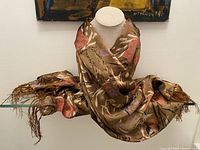 Full view of the brown silk scarf draped on a mannequin showing overall color, print design, and 4-inch fringe ends.