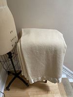 Full view of the cream wool blanket draped over a wooden stand and near a dress form, showing the overall color, texture, and style.