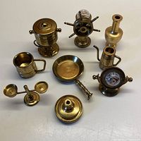 Full overhead view of all 10 miniature brass items neatly arranged on white surface showing variety and detail of items.