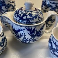 Close-up of porcelain teapot featuring blue foliage decoration and fitted lid with knob and spout.